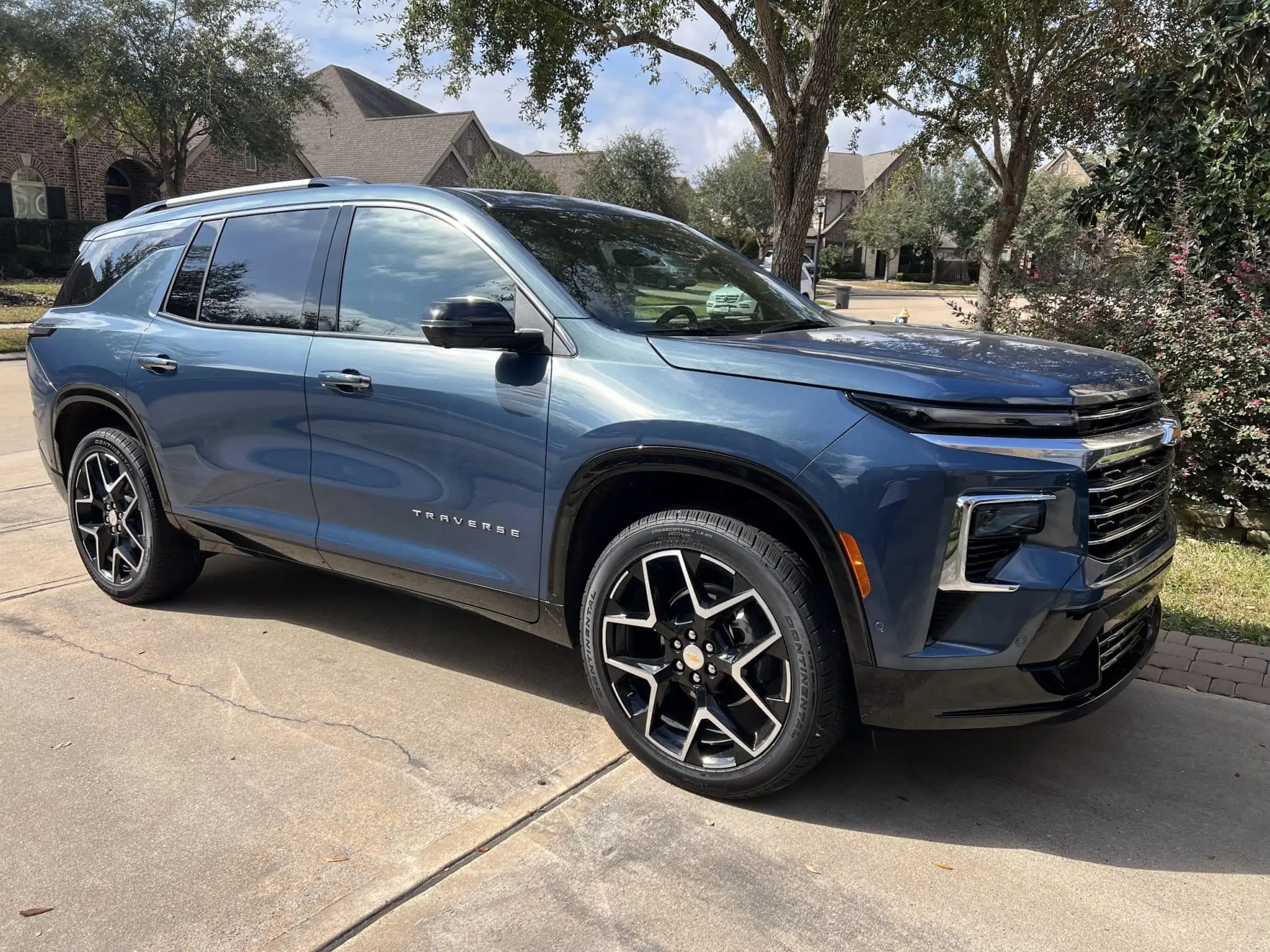 Blue 2023 Chevrolet Traverse SUV parked on driveway with trees and houses in background.